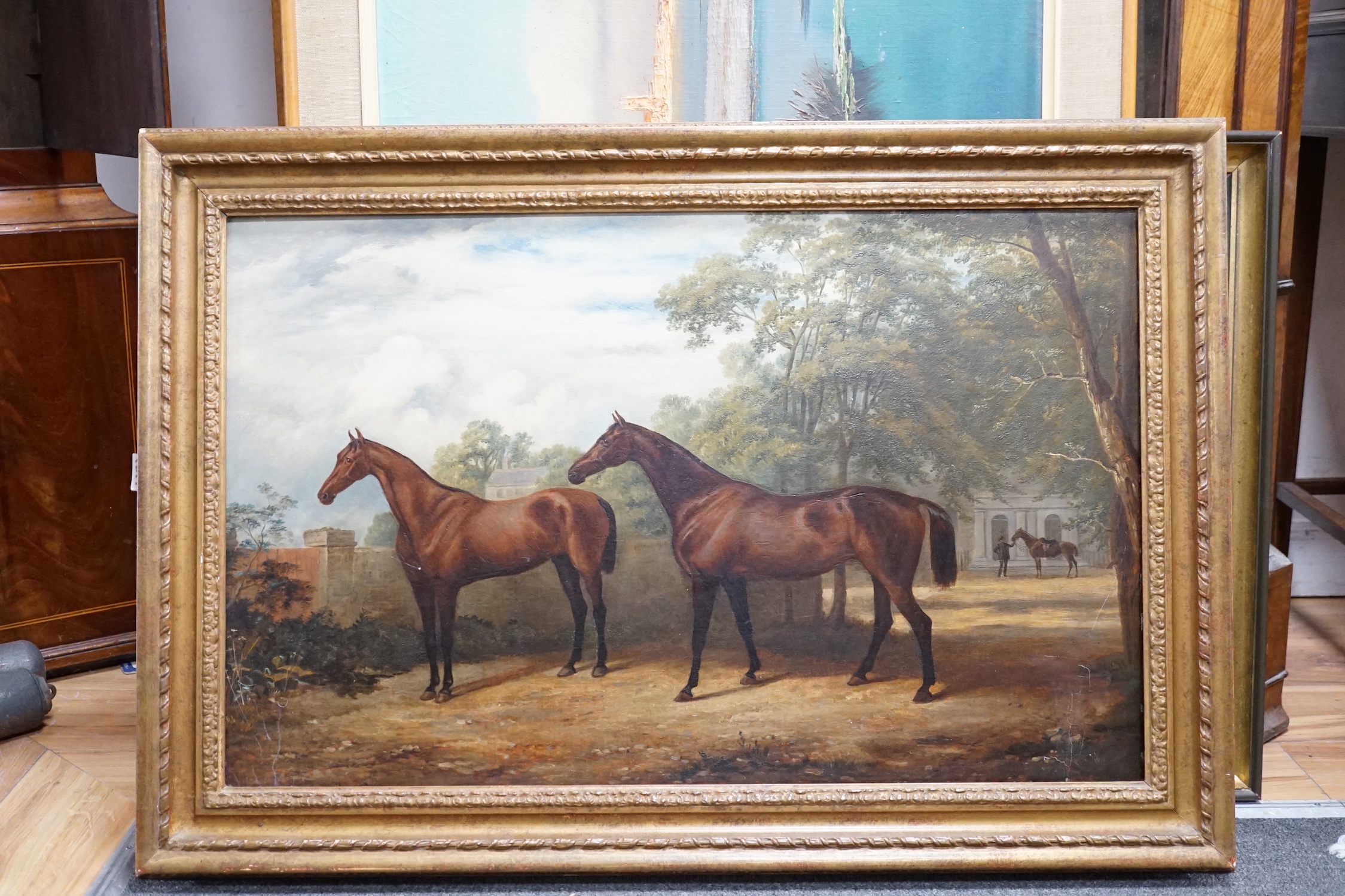 English School c.1900, oil on canvas, Portrait of two racehorses standing in parkland, a groom and another horse beyond, 48 x 76cm